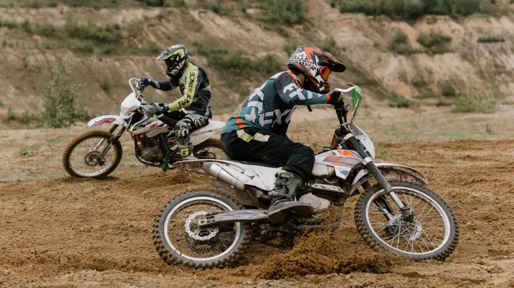 Two riders on competition dirt bikes on a dirt track