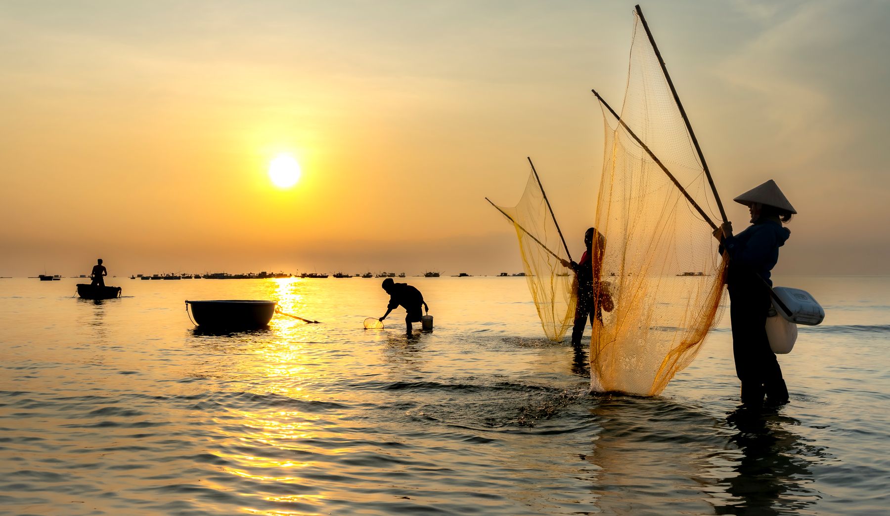 A fisherman casting a net on calm water at sunrise