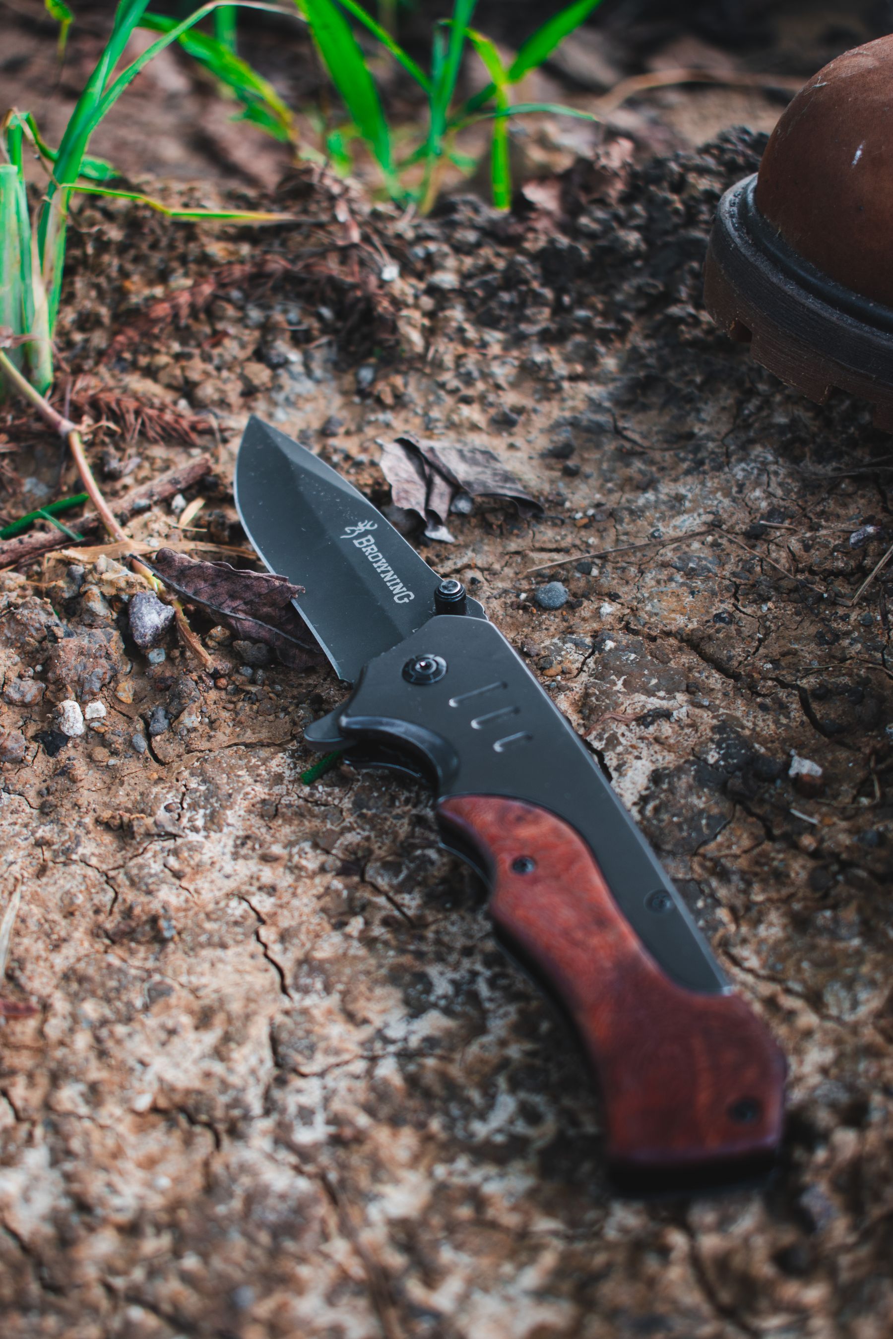 A folding knife with a wooden handle resting on the forest floor