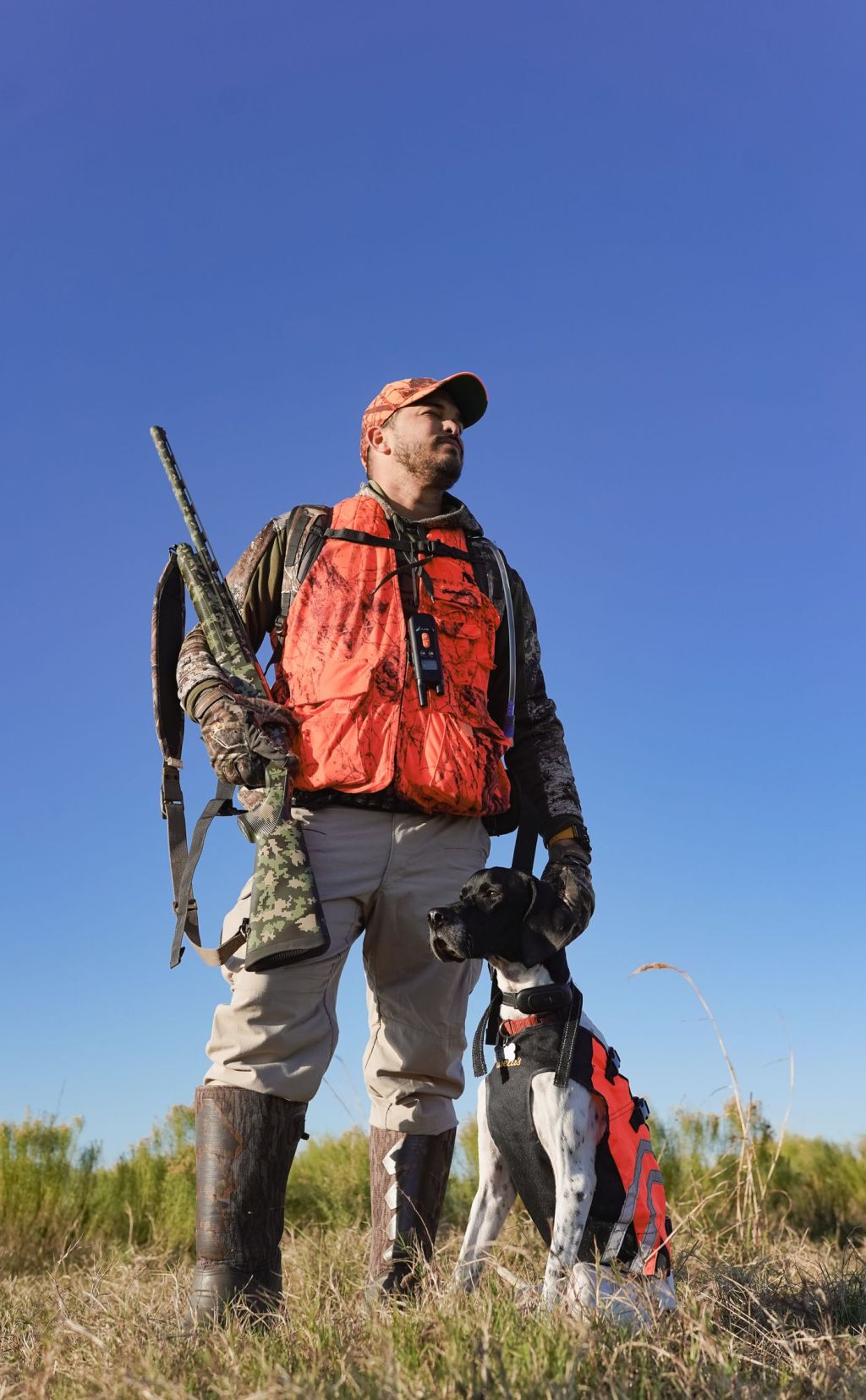 A hunter in a blaze orange vest and cap carrying a rifle