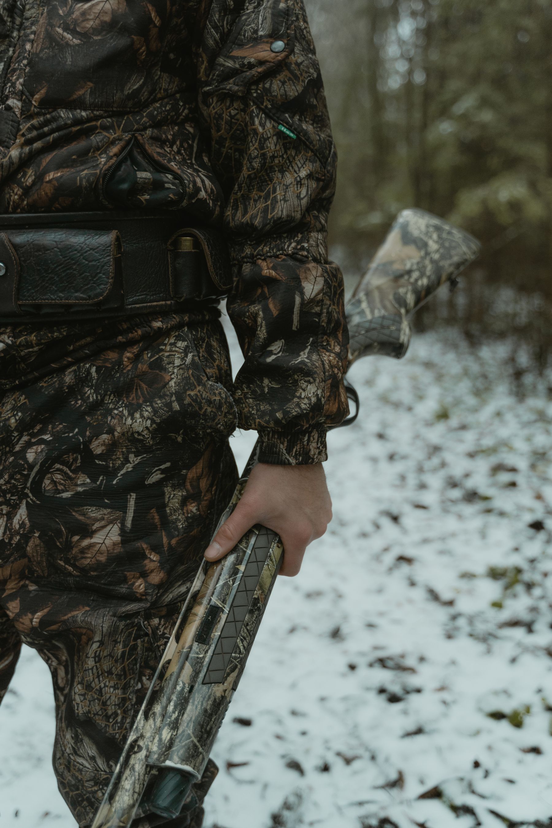 A hunter in camouflage holding a shotgun in a snowy field