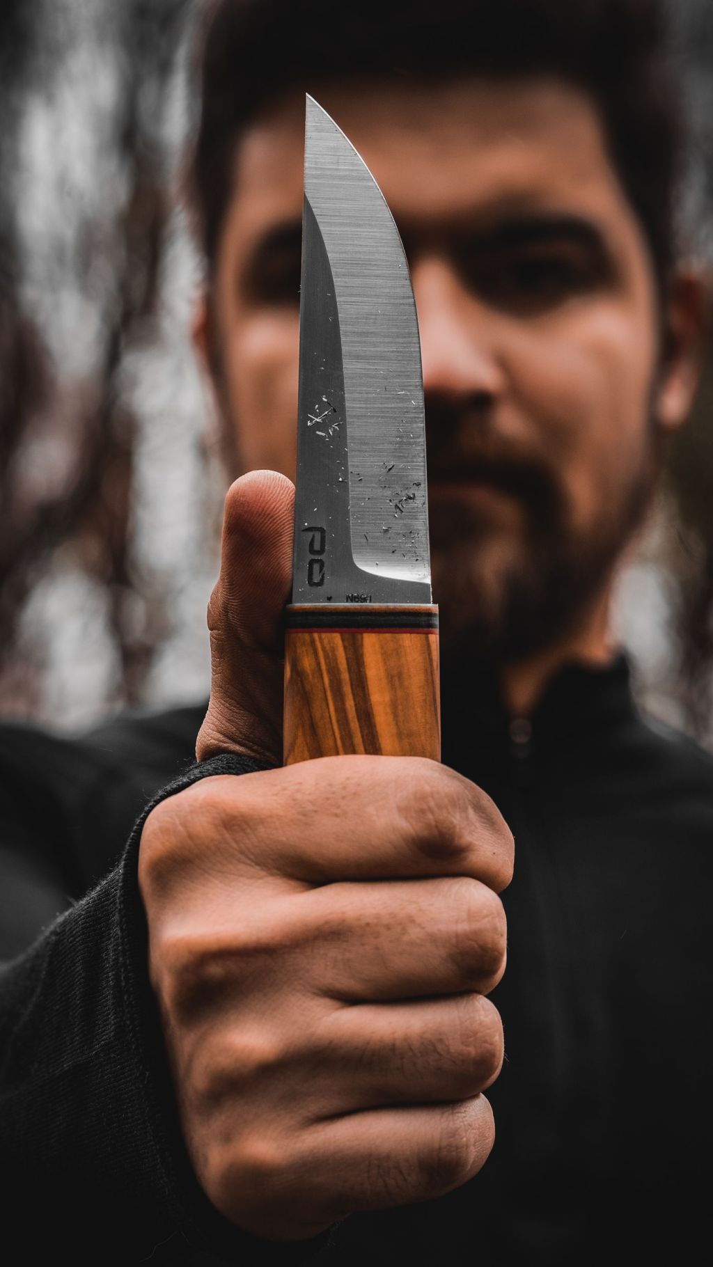 A person holding a sharp knife blade in a forest setting