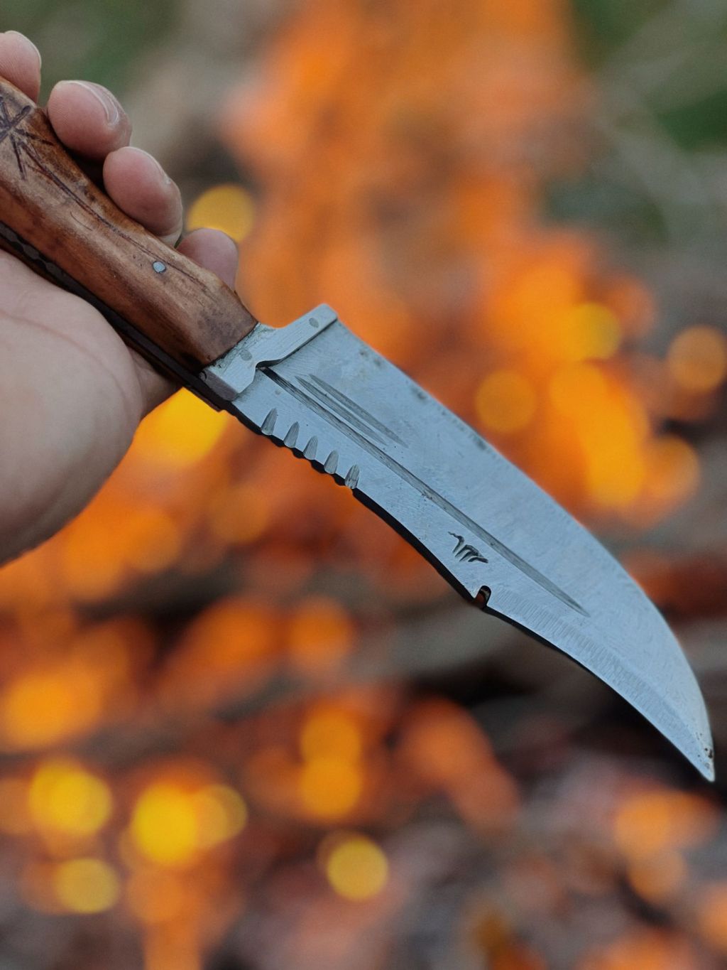 A person holding a fixed-blade knife beside a campfire