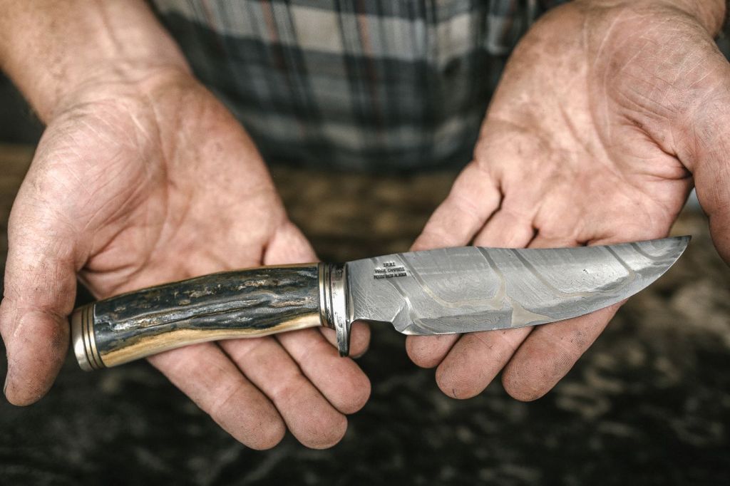 A hand gripping a fixed-blade knife with a horn handle
