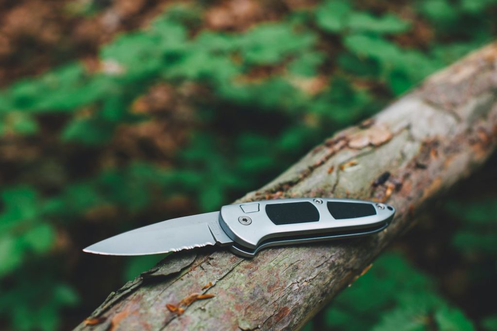A folding knife resting open on a mossy branch
