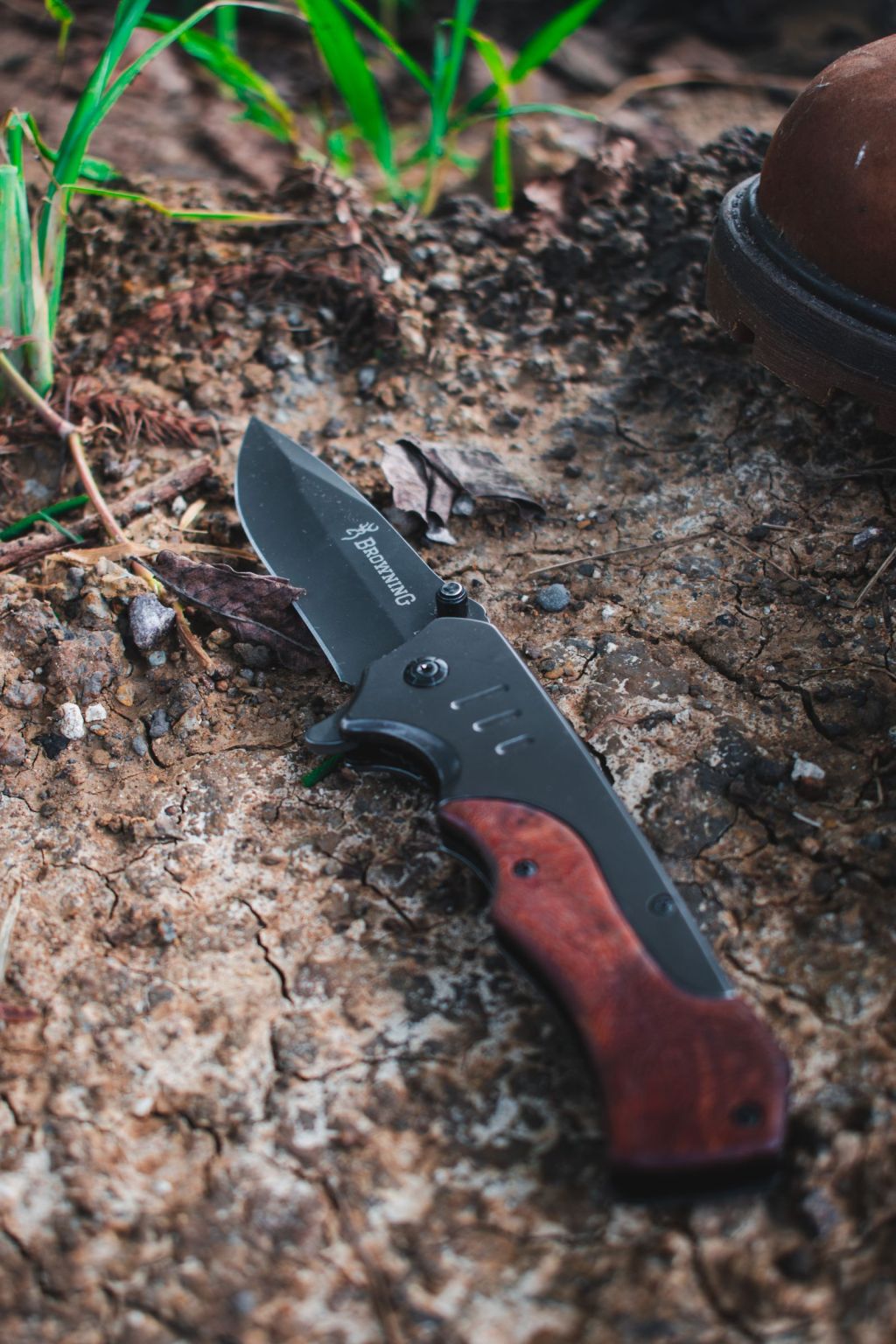 A folding knife with a wooden handle lying on the ground among leaves