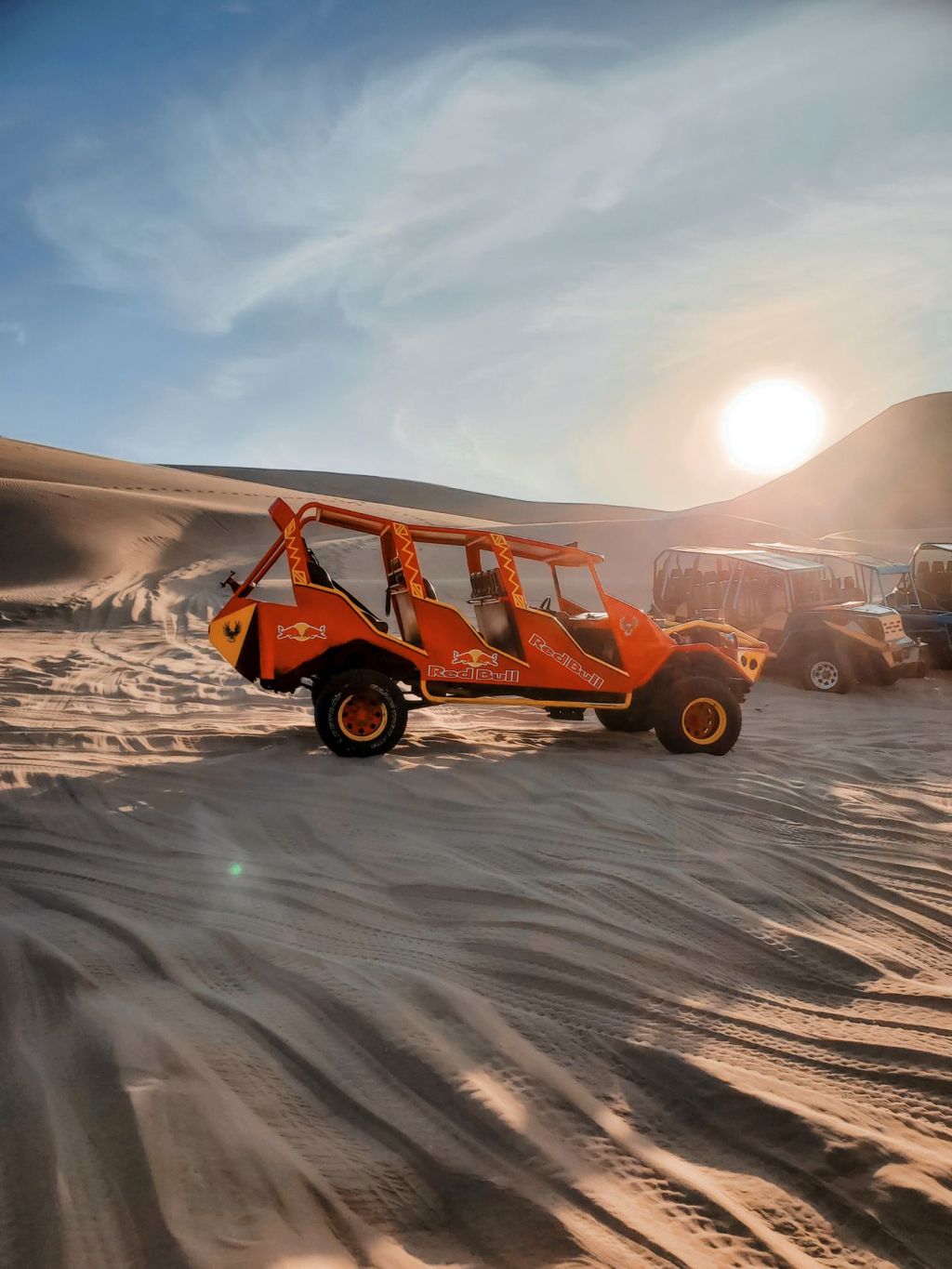 An off-road buggy driving across sand at sunset