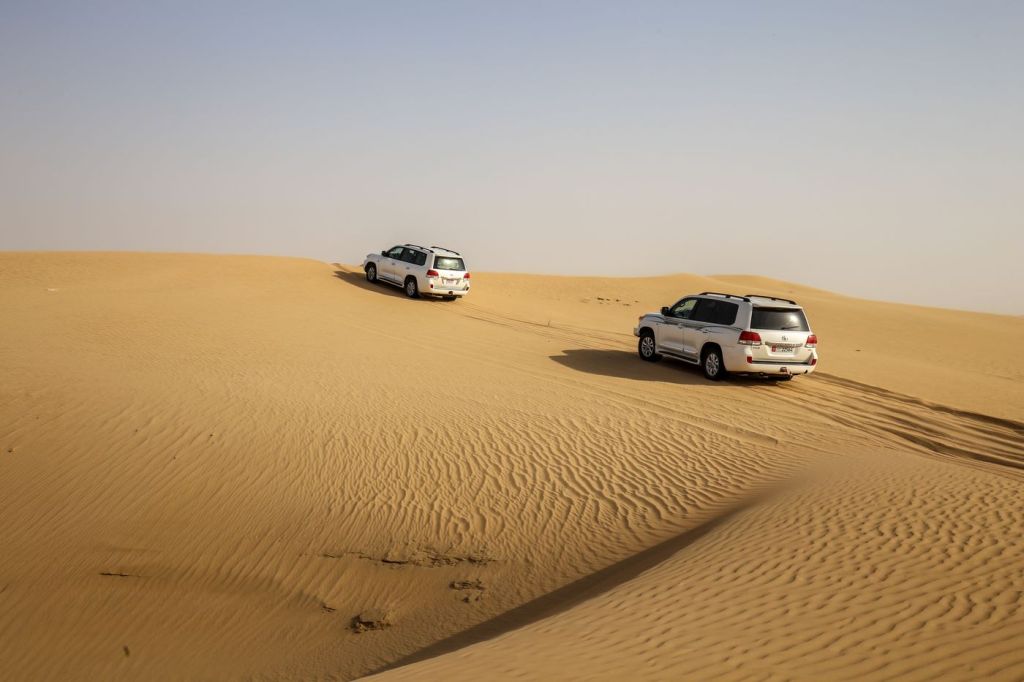 Two vehicles crossing sand dunes