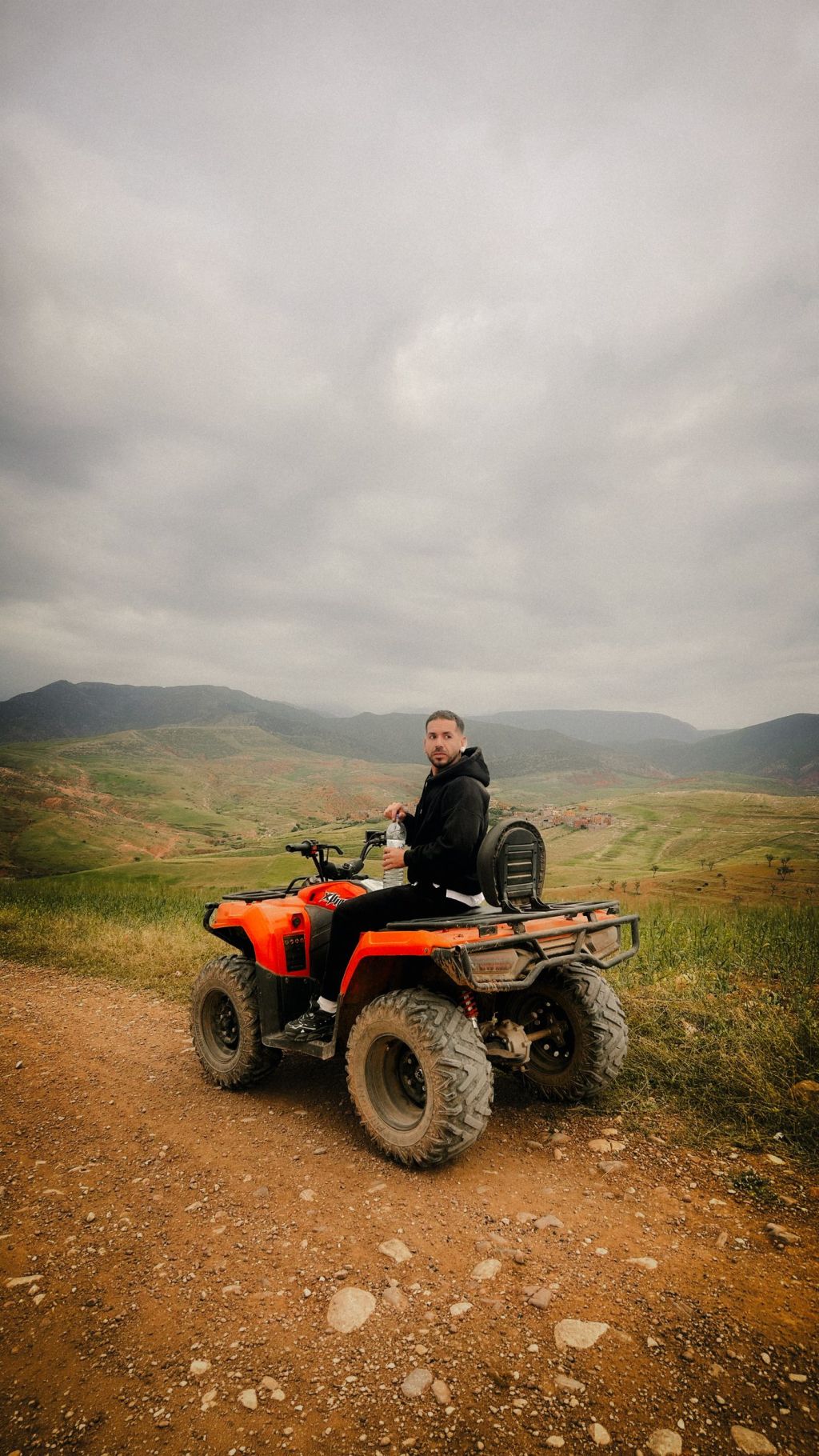 A rider on an ATV on a mountain trail under cloudy sky