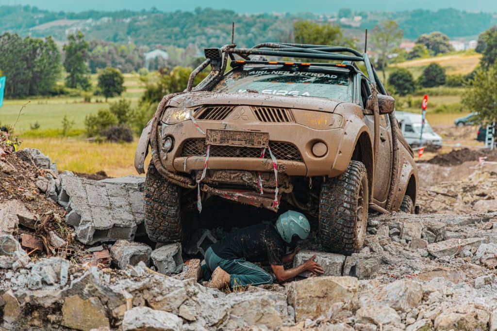 A four-wheel drive climbing rocky terrain with a person on the ground guiding the driver
