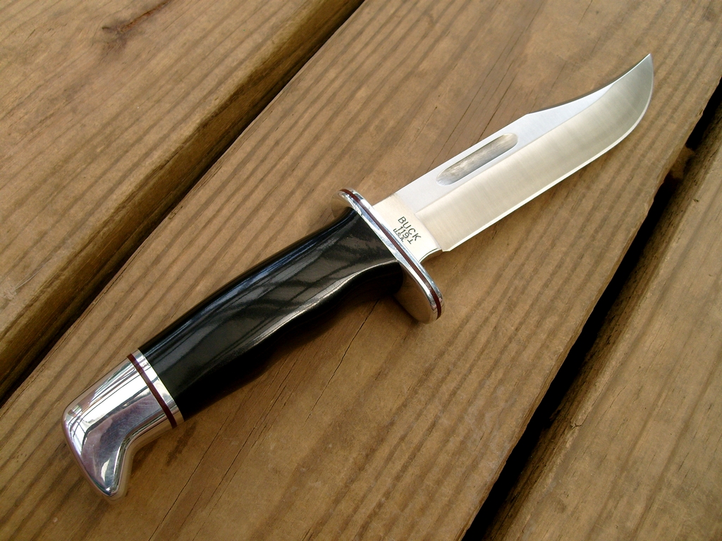 A fixed-blade hunting knife with a dark handle on wooden boards