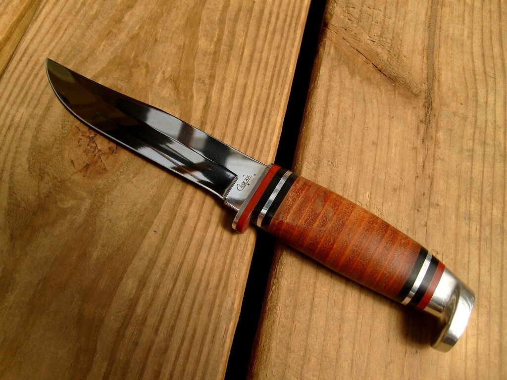 A fixed-blade knife with a stacked leather handle on wooden boards