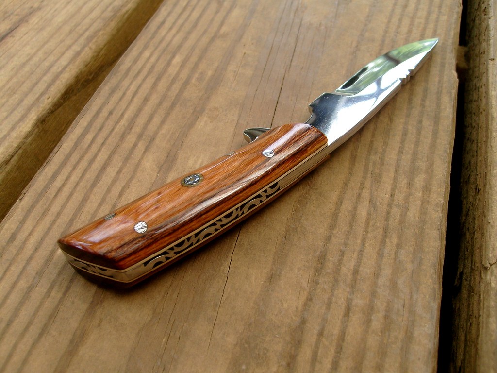 A folding knife with a wooden handle open on a wooden surface