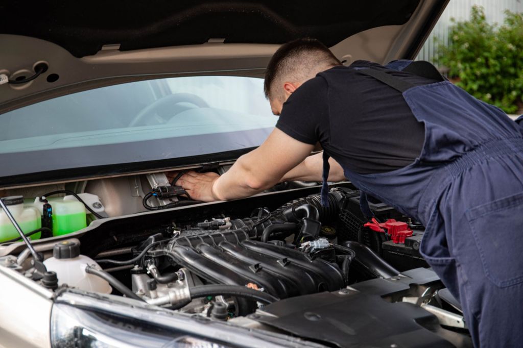 A technician working under the open hood of a vehicle in a service bay