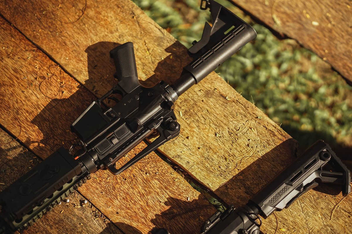 An AR-style rifle lying on weathered wooden planks in natural light